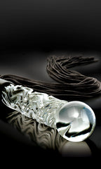 A clear glass or acrylic textured wand with a large spherical end, shown on a glossy black reflective surface with a dark brown velvet ribbon behind it.