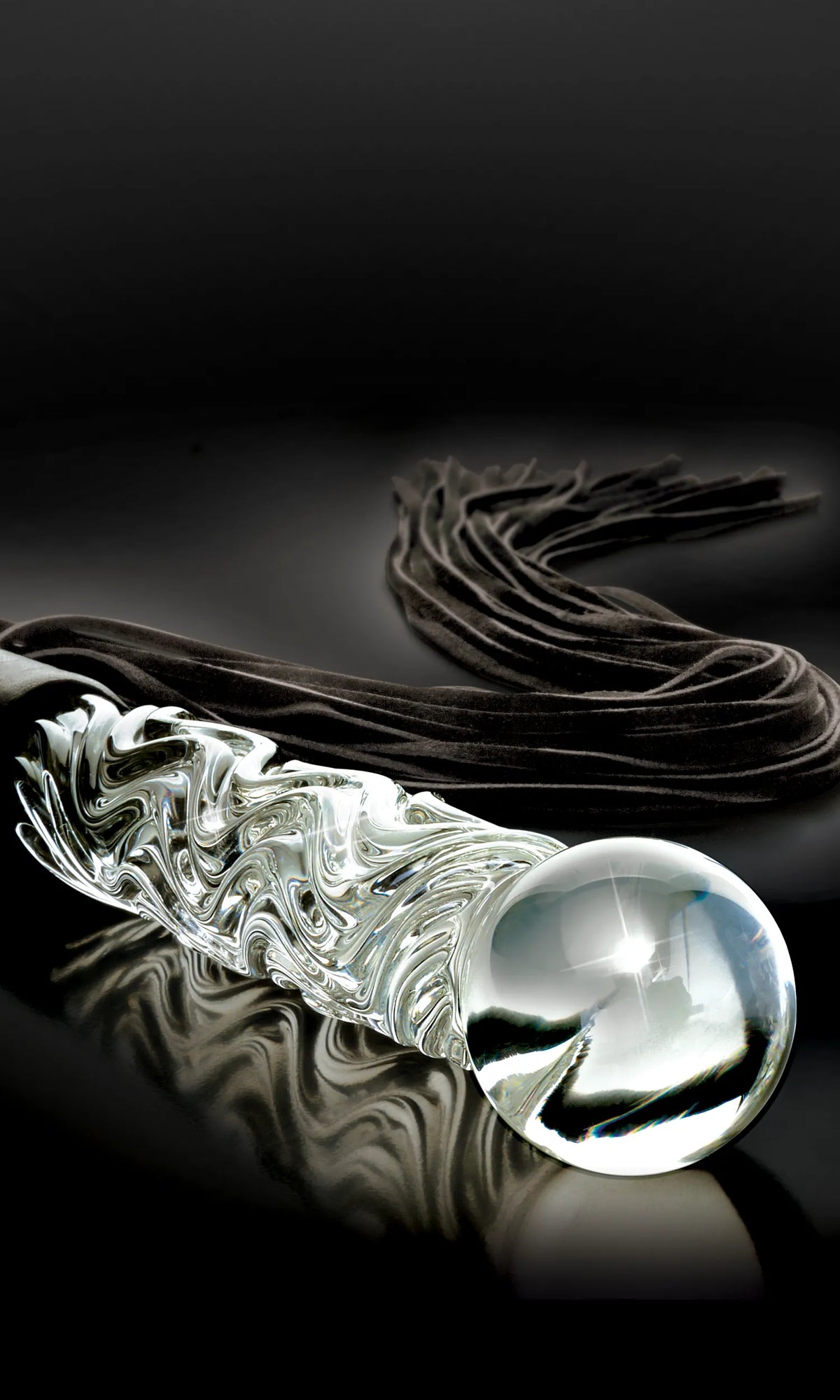 A clear glass or acrylic textured wand with a large spherical end, shown on a glossy black reflective surface with a dark brown velvet ribbon behind it.